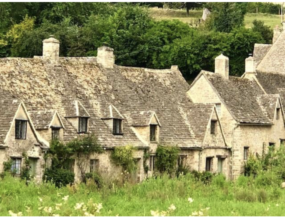 A village with charming houses in a green field in the Cotswolds, England
